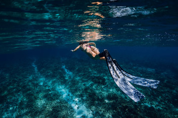 Woman freediver with fins glides over coral reef.