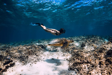 Woman freediver glides underwater with sea turtle.