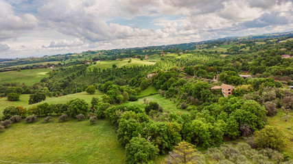 Fototapeta na wymiar Awesome aerial view with green hills and meadows, oaks forest and agriculture fields planted with fruit trees with dramatic sky