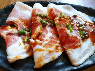 Top view of pork belly or kurobuta bara with scallion sliced and spicy sauce in black plate on wooden table in restaurant at Thailand, fresh meat for grill