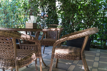 Fototapeta na wymiar tables and wicker chairs in outdoor summer cafe with flower beds