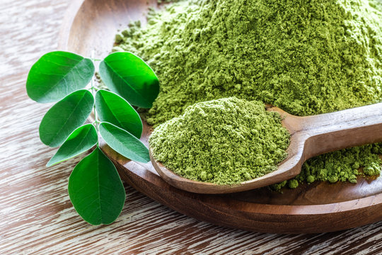 Moringa powder (Moringa Oleifera) with original fresh Moringa leaves on rustic background.