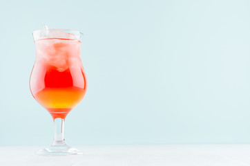 Alcohol juicy fruit red cocktail with red and yellow liquor in wineglass in modern elegant pastel blue interior.