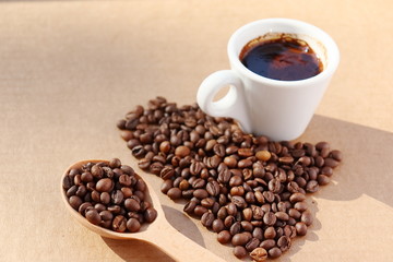 Spilled coffee. Grains of aromatic roasted coffee scattered in the form of a heart on a cardboard surface in the rays of the rising sun.