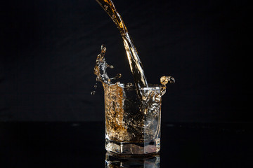 Whiskey pouring into glass with ice isolated on black background..