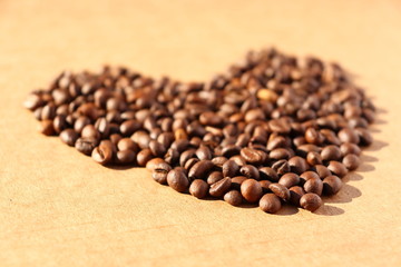 Spilled coffee. Grains of aromatic roasted coffee scattered in the form of a heart on a cardboard surface in the rays of the rising sun.