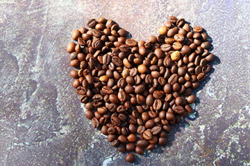 Spilled coffee. Grains of aromatic roasted coffee scattered in the form of a heart on a cardboard surface in the rays of the rising sun.