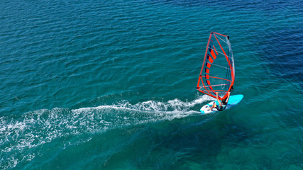Aerial top view photo of fit man practising wind surfing in Mediterranean bay with crystal clear emerald sea
