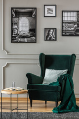 Pillow on emerald green armchair in elegant living room with black and white photos on grey wall