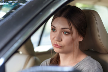 Young attractive caucasian woman behind the wheel driving a car with grimace of disappointment, frustration or displease. Strong emotions, duck face. Copy space.