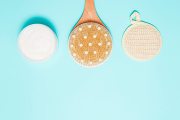 Body massage brush with cream on blue background. Massage brush for the body. Skin care products. Spa massage brush with natural bristles for body peeling or anti-cellulite massage. Top view.