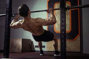 Fototapeta na wymiar Athlete muscular fitness male model pulling up on horizontal bar in a sport-club.
