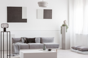 Trendy living room interior with white wall, painting and grey settee