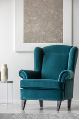 Blue velvet armchair in elegant white interior with abstract silver painting on the wall