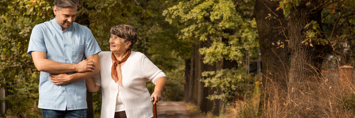 Panoramic view of grey senior lady with walking cane in the garden with volunteer
