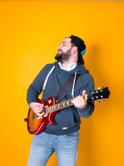 Obraz premium man with black hair and beard, wearing grey hoodie playing the electric guitar in front of a yellow background