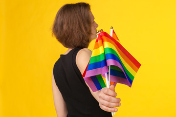 Young unrecognizable woman  holding small LGBT flag on bright color background