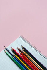 Notepad with color pencils on pink background with copy space