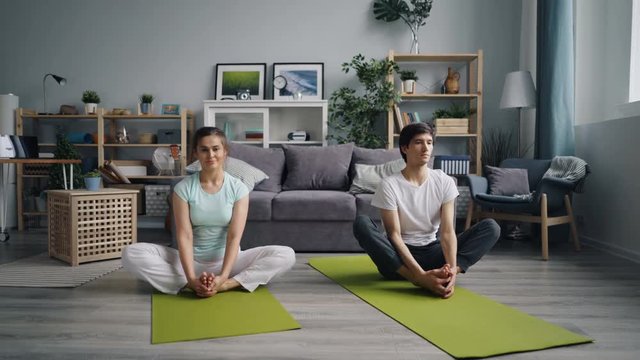 Husband and wife healthy young people are stretching body and legs at home then relaxing in butterfly position sitting on floor on yoga mats. Youth and sports concept.