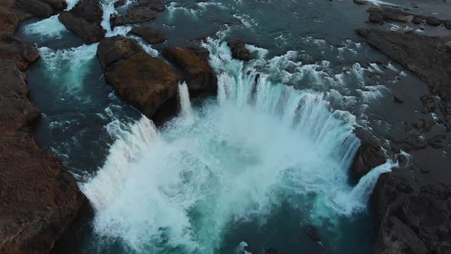 The extremely popular waterfall Godafoss filmed from above in a close view with the blue water falling down between the rocks in a half circle with great power making the water foam