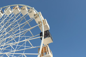 Close-up big white modern ferris wheel against clear blue sky on background in Kiev city center. One black gondola among other. One of a kind