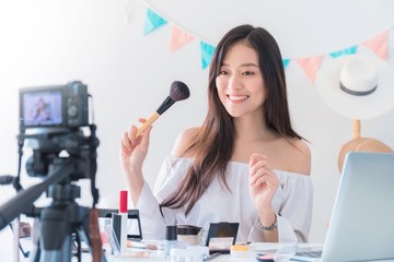 Asian beautiful woman blogger is showing how to make up and use cosmetic. In front of the camera to recording vlog video live streaming at home.Business online influencer on social media concept.