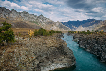 Fototapeta premium Turquoise Katun river in gorge is surrounded by high mountains under majestic autumn sky. A stormy mountain stream runs among rocks - landscape of the Altai mountains, beautiful places of the planet.