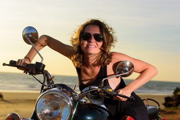 Fototapeta na wymiar Sexy blonde woman in sunglasses smiling and grimacing while sitting on the motorbike. Bright emotions on vacation.