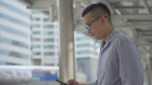 Slow motion portrait asian businessman texting with friend on smartphone at urban city background, Searching for social media.