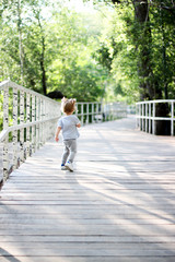 The child runs through the woods on a wooden bridge. The child walks in the park