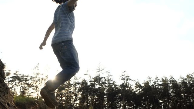 Man jumps in a sand in slow motion outdoors at sunset.