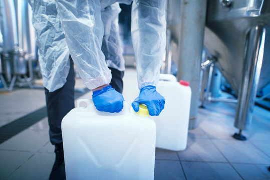 Shot of an unrecognizable industrial worker technologist with protective rubber gloves opening plastic can with chemicals in factory.