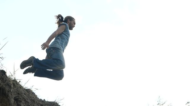 Man jumps in a sand in slow motion outdoors at sunset.