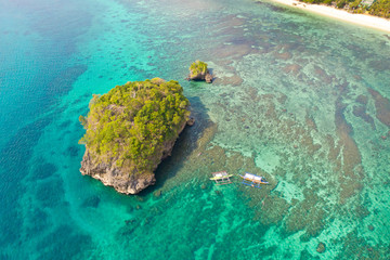 Small rocky island in the blue lagoon, view from above. Bay with turquoise water and coral bottom.