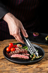 Chef hands serving meat steak and vegetables assorted cooked on grill.