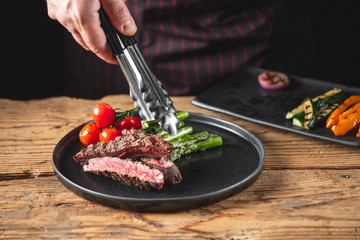 Chef hands serving meat steak and vegetables assorted cooked on grill.