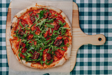Neapolitan spicy pizza with ham, cheese, arugula, basil, tomatoes, pepperoni pepper sprayed with cheese on a wooden board on a tablecloth in a cell with a place for text