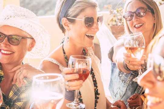 Closeup of happy beautiful cheerful people women celebrating together with red wine - bright sunny image joyful and friendship - young senior ladies smiling and laughing having fun at party