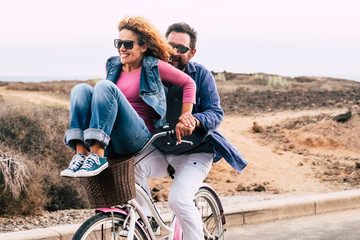 Cheerful caucasian people having fun together in friendship and relationship - adults couple laugh a lot both on a bike enjoying the outdoor leisure activity