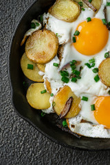 Breakfast fried eggs with fried potatoes, green onions on a cast iron pan