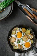 Fried eggs with fried potatoes, green onions on a cast iron pan