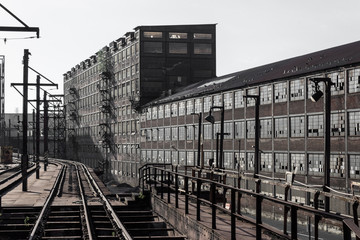 Long view of train tracks alongside expansive warehouses of brick with walls of windows, industrial complex, horizontal aspect