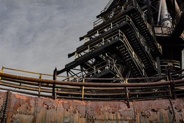 Rusting metal pipe structure with graduating stairs, exterior steel mill complex, copy space, horizontal aspect