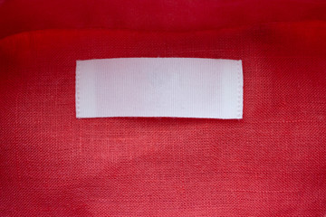 White blank clothing tag label on red linen shirt fabric texture background