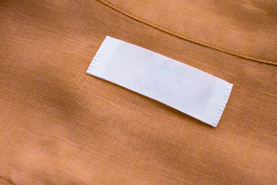 White blank clothing tag label on brown linen shirt fabric texture background
