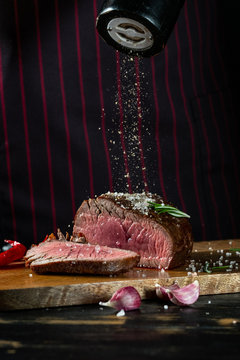 Cooking juicy beef steak by chef hands on dark black background with copy space for text menu or recipe.