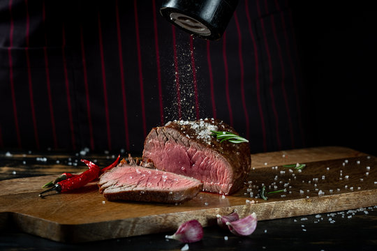 Cooking juicy beef steak by chef hands on dark black background with copy space for text menu or recipe.