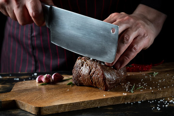 Slicing juicy beef steak slicing by knife in chef hands closeup. Food cooking concept. Dark black background copy space.