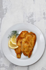 fried chicken with lemon on white plate on ceramic background