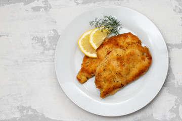 fried chicken with lemon on white plate on ceramic background